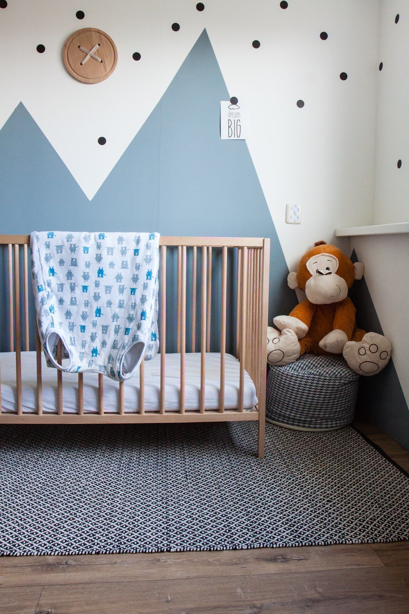 Babykamer met ledikantje en blauwe bergen geverfd op de muur.