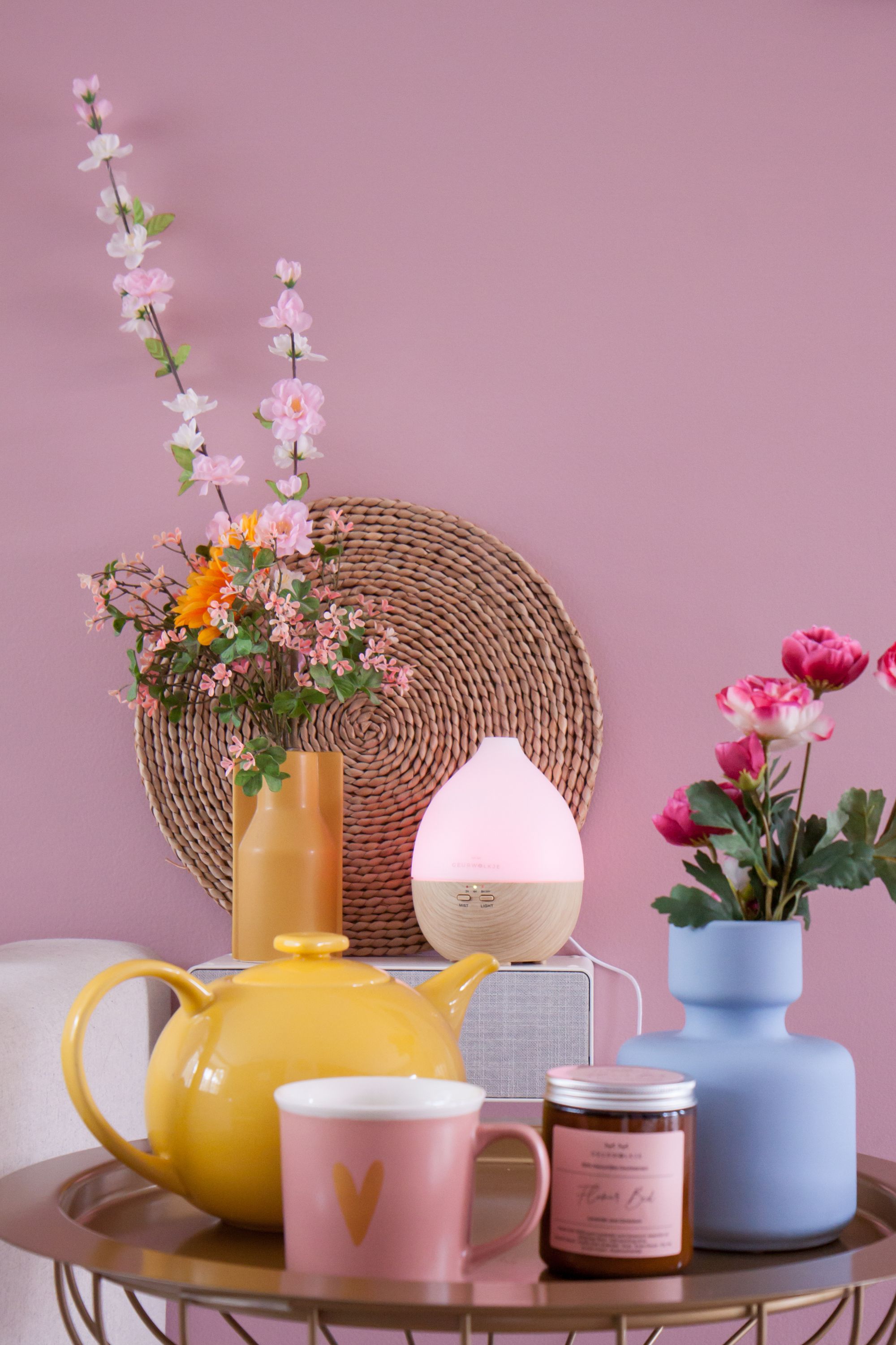 Sfeerplaatje met een geurkaars, aroma diffuser, bloemen en thee.