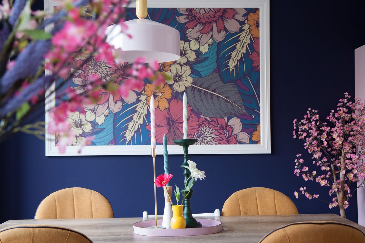 Eetkamer met donkerblauwe muur, eettafel met gele stoelen en kaarsen op tafel
